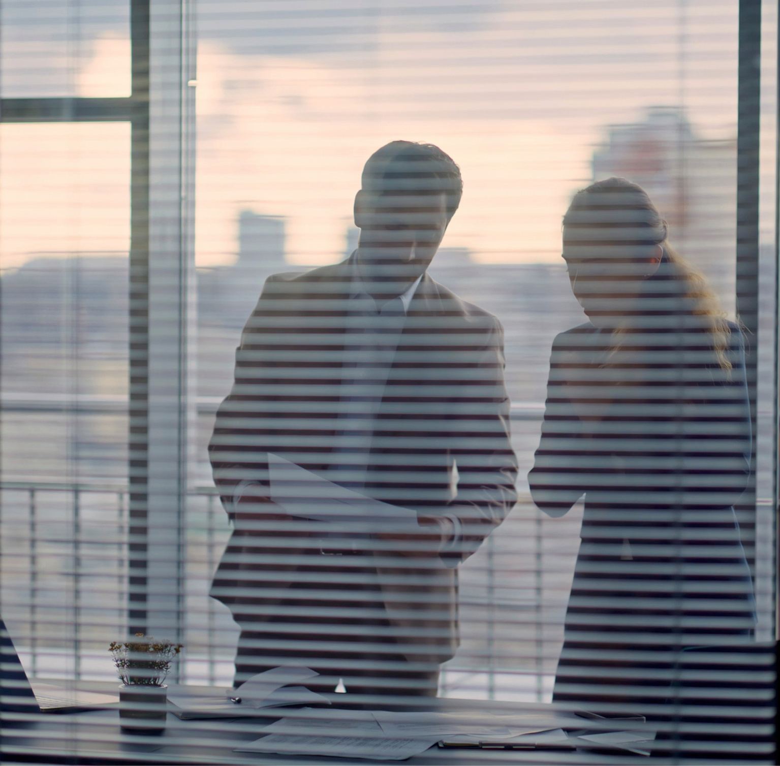 Two colleagues seen through window blinds